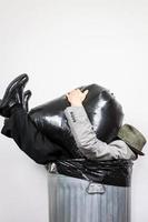 homme d'affaires assis dans la poubelle peut être écrasé par un sac poubelle. concept de plus d'un baril. battus et noyés dans les déchets. photo