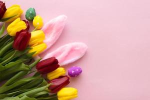 belles tulipes, oeufs de pâques décorés et oreilles de lapin sur fond rose de couleur, vue de dessus