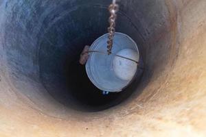 Vieux puits avec seau en fer sur longue chaîne forgée pour l'eau potable photo