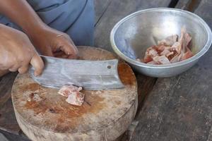 la main du cuisinier tient le couteau hacher le poulet sur une planche à découper en bois pour cuisiner dans une cuisine de campagne. photo