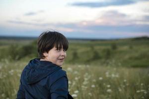 un portrait d'un enfant joyeux avec les émotions positives des enfants se tient à moitié tourné, jouant dans la nature. enfant heureux, mode de vie. produits pour enfants. photo