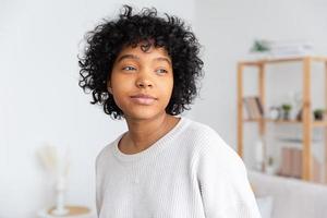 belle fille afro-américaine avec une coiffure afro à la maison à l'intérieur. jeune femme africaine aux cheveux bouclés dans le salon. beauté ethnique, concept de vie domestique. photo