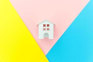concevoir simplement avec une maison de jouet blanche miniature isolée sur fond géométrique à la mode bleu jaune rose pastel coloré concept de maison de rêve d'assurance de propriété hypothécaire. espace de copie plat vue de dessus. photo