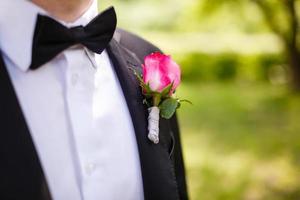 homme en costume gris corrige la main d'une boutonnière rose rouge photo