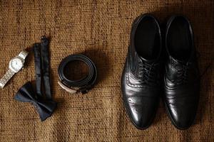 chaussures noires, ceinture noire, montre noire, papillon noir, boutons de manchette et parfum sur fond marron avec limogeage