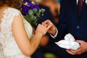 les jeunes mariés échangent des bagues, le marié met la bague sur la main de la mariée au bureau d'enregistrement des mariages photo