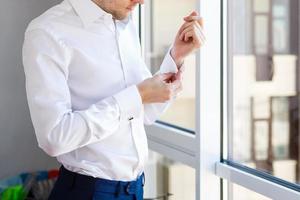 l'homme boutonne sa chemise blanche debout devant une fenêtre lumineuse photo