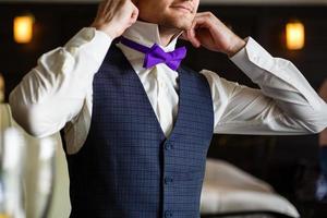 papillon de couleur violette sur un cou chez l'homme. l'homme porte un nœud papillon violet et violet. l'époux va au mariage. matin de mariage. l'homme redresse sa cravate. photo