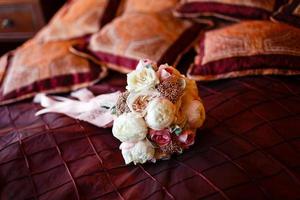 bouquet de mariage se trouve entre des oreillers rouges sur le canapé photo