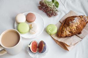 esthétique d'une tasse de café, de figues, d'un grand croissant et de macarons sur fond blanc, vue de dessus photo