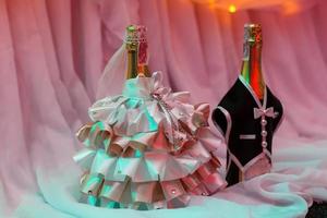 deux bouteilles de champagne de mariage, décorées dans les vêtements des mariés. décorations sur la table nuptiale pour les jeunes mariés au banquet. photo