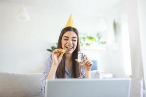 fête virtuelle. femme heureuse en chapeau de fête célébrant son anniversaire en ligne en quarantaine ou en auto-isolement, utilisant un ordinateur portable pour un appel vidéo avec des amis et la famille, tenant du champagne photo