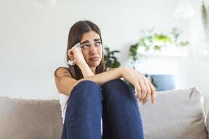 jeune femme malheureuse couvrant le visage avec les mains, pleurant seule en gros plan, fille déprimée assise sur un canapé à la maison, problème de santé ou pensant à de mauvaises relations, rompre avec son petit ami, divorcer photo