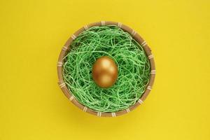 oeuf d'or dans un panier en osier de rotin en bois sur fond jaune. concept d'entreprise d'investissement financier. composition de conception festive de chasse aux oeufs de pâques. vue de dessus, mise à plat. journée mondiale de l'œuf. fermer photo