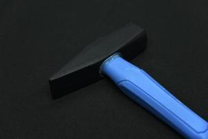 marteau de construction sur fond noir. un marteau de charpentier avec un manche bleu sur fond noir. photo