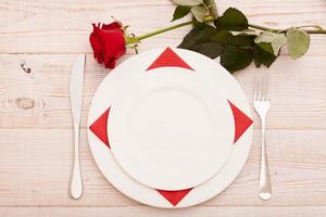 vue de dessus de la vaisselle d'une assiette vide ronde et en forme de coeur, d'un couteau et d'une fourchette en métal servis sur une table en bois blanc avec une bougie rougeoyante et une boîte cadeau préparée pour la célébration de la saint valentin