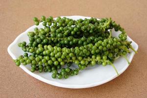 jeunes fruits verts de poivre thaïlandais sur plaque blanche. fond en bois marron. concept, épices à base de plantes pour la cuisine, l'ingrédient alimentaire peut être cuit dans de nombreux menus thaïlandais. photo