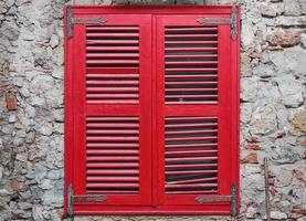 des stores en bois rouges ferment la fenêtre sur le vieux mur de pierre de la maison. vieux mur de briques, idée pour studio intérieur ou loft et cour photo