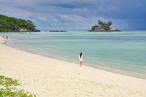 mahe seychelles, jeune femme sur la plage royale faisant des photos, océan clair et calme avec île à l'arrière photo