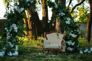 belle cérémonie de mariage en plein air. des chaises décorées se tiennent sur l'herbe. arche de mariage en tissu et fleurs blanches et roses sur fond vert naturel. vieilles portes, style rustique. photo