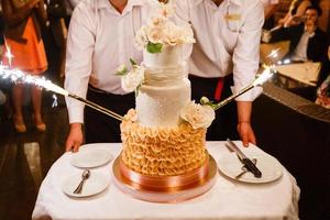 la mariée et le marié heureux coupent le gâteau de mariage devant les feux d'artifice photo