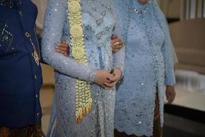 parents tenant leur belle mariée portant une robe de mariée avec un collier de fleurs de jasmin et de magnolia pour une cérémonie de mariage traditionnelle en indonésie photo