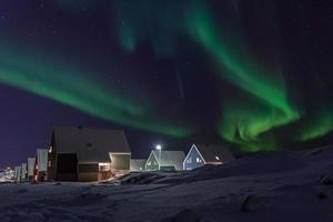 village arctique et vagues vertes d'aurores boréales au-dessus des maisons inuites, dans la banlieue de nuuk, groenland photo