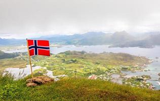 drapeau national norvégien dans le vent au sommet du pic nonstinden avec fjord en arrière-plan, ballstad, municipalité de vestvagoy, comté de nordland, norvège photo
