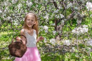 adorable petite fille avec un panier de paille dans un verger de pommiers en fleurs photo