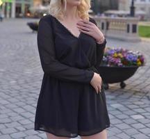 belle mannequin blonde portant une robe noire courte et des talons hauts fait une séance photo dans la rue
