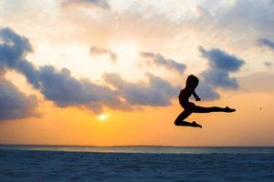 silhouette d'adorable petite fille active sur la plage blanche au coucher du soleil photo