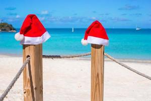 gros plan deux chapeaux de père noël sur une clôture sur une plage blanche tropicale photo