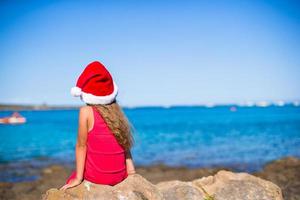 vue arrière de la mignonne petite fille en bonnet de noel sur la plage photo