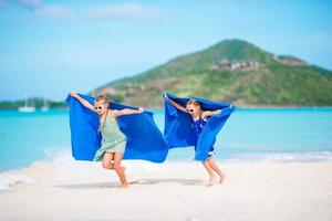 jolies petites filles s'amusant à courir avec une serviette et profitant de vacances sur une plage tropicale avec du sable blanc et de l'eau turquoise de l'océan photo