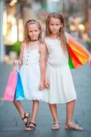 adorables petites filles sur le shopping. portrait d'enfants avec des sacs à provisions dans une petite ville italienne photo