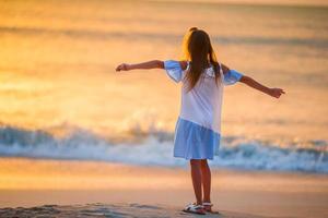 adorable petite fille heureuse marchant sur la plage blanche au coucher du soleil. photo