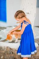 petite fille adorable jouant avec un chat roux dans un village grec en plein air photo