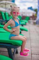 petite fille heureuse sur les transats au bord de la piscine en regardant la caméra photo