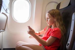 adorable petite fille voyageant en avion. enfant écoutant de la musique assis près de la fenêtre de l'avion photo