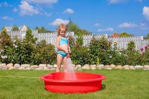 petite fille heureuse versant de l'eau d'un tuyau et riant photo