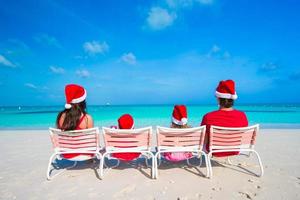famille heureuse de quatre personnes sur la plage en chapeaux rouges de santa photo