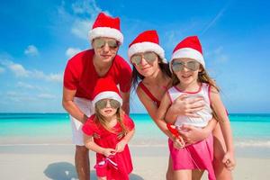 portrait de famille heureuse en chapeaux de père noël sur la plage photo