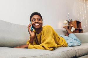 femme africaine utilisant un téléphone portable à la maison assise sur le canapé photo