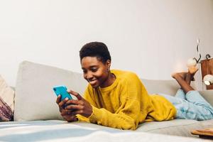 femme africaine utilisant un téléphone portable à la maison assise sur le canapé photo