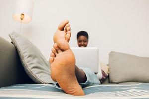 Close up pieds de femme noire à l'aide de son ordinateur portable sur un canapé photo