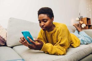 femme africaine utilisant un téléphone portable à la maison assise sur le canapé photo