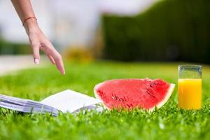 tranche de pastèque rouge mûre, verre de jus d'orange et livre sur l'herbe verte photo