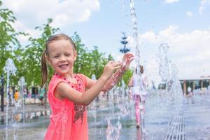 petite fille heureuse s'amuser dans la fontaine de la rue lors d'une chaude journée ensoleillée photo