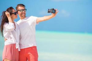 couple heureux prenant une photo sur la plage blanche en vacances de lune de miel