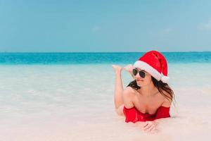 jeune femme en bonnet de noel marchant écarta les mains sur la plage de sable blanc photo